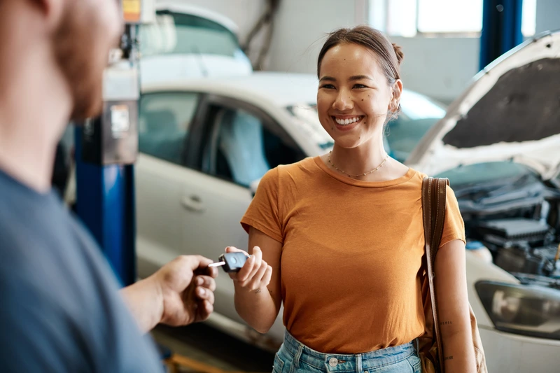 Service advisor handing car keys to a smiling customer in a repair shop